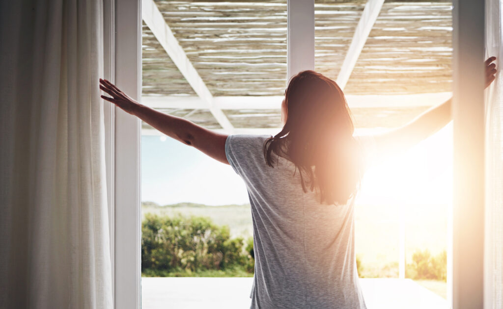 woman opening up curtains getting ready for her daily routine